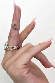 a woman's hand with pink nails and a ring on her finger, showing the moon tattoo