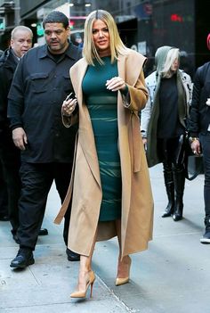 a woman in a green dress and trench coat is walking down the street with another man