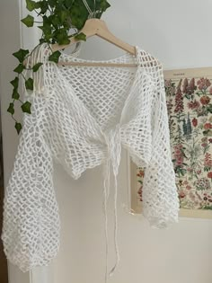 a white crocheted shawl hanging on a wooden hanger next to a wall