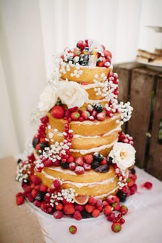 a multi layer cake with berries and flowers on it's top is sitting on a table