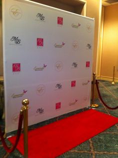 a red carpeted area with a white backdrop and gold poles on the side, along with a red carpet