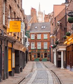 an empty cobblestone street with buildings in the background and a yellow sign hanging from it's side