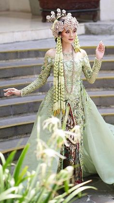 a woman dressed in an elaborate green gown and headdress stands on some steps