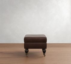 a brown foot stool sitting on top of a wooden floor next to a white wall