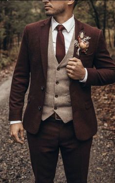 a man in a suit and tie standing on a dirt road with trees in the background