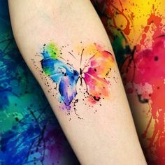 a colorful butterfly tattoo on the left forearm and leg, with watercolor paint splatters all over it