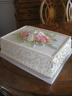 a white cake with pink flowers on it sitting on top of a wooden dining room table