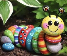 a colorfully painted caterpillar sitting on top of rocks in front of some plants