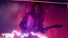 a woman with long hair holding a guitar in front of a neon light on her body