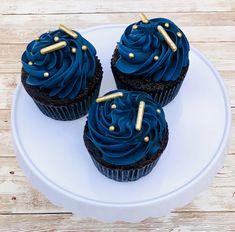 three cupcakes with blue frosting and gold sprinkles on a white plate