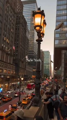 people are walking on the sidewalk next to a street light in new york city at dusk