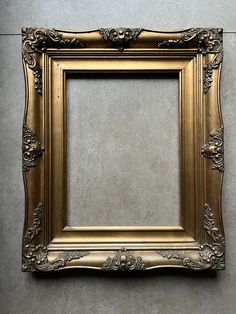 an ornate gold frame hanging on the wall with a gray cement floor and grey walls behind it