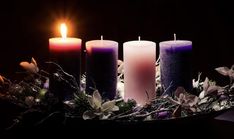 three lit candles sitting on top of a table with greenery and flowers around it