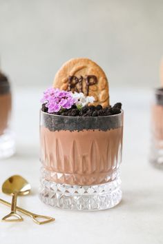 there is a dessert in the glass with chocolate and flowers on it, next to two spoons