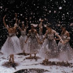 a group of women in white dresses standing on snow covered ground with their arms raised