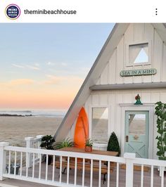 a small white house on the beach with an orange surfboard in front of it