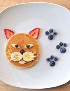 a white plate topped with pancakes covered in fruit and cat face cutouts on top of it