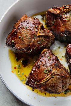 three pieces of cooked meat in a white bowl with sauce and garnish on the side