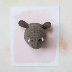 a stuffed animal head mounted to the wall on a pink and white background with watercolor stains