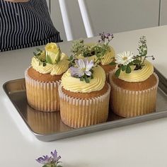 three cupcakes on a tray with flowers in them