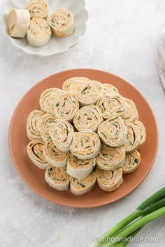 a plate filled with rolls on top of a table next to green onions and other food items