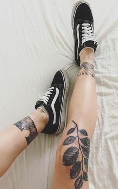 a woman's legs with tattoos on them sitting on a white sheet and wearing black vans