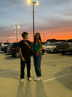 two people standing in a parking lot at sunset