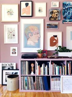 there are many pictures on the wall and bookshelf in this living room with pink walls