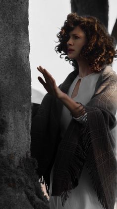 a woman standing next to a tree wearing a shawl and holding her hands out