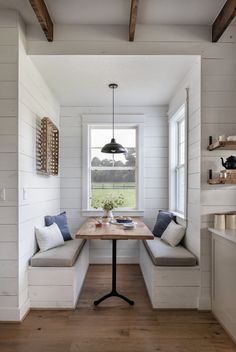 a kitchen with white walls and wood flooring has a window seat on the far side