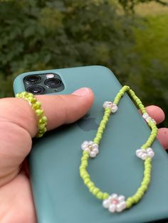 a hand holding a cell phone with a green beaded necklace on the back of it