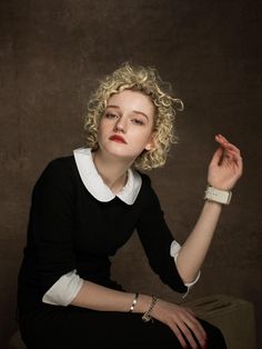 a woman sitting on top of a stool wearing a black dress and white collared shirt