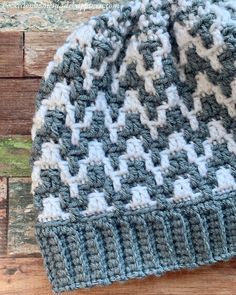 a blue and white crocheted hat sitting on top of a wooden table next to a piece of wood