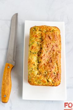 a white plate topped with a loaf of zucchini bread next to a knife