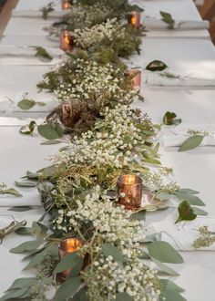 a long table with candles and greenery on the top is set up for a wedding reception