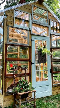 a small greenhouse with lots of windows and plants in the front, surrounded by greenery