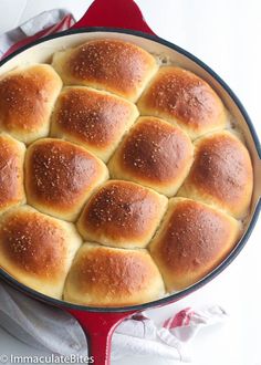 a pan filled with bread rolls on top of a white and red table cloth next to a knife