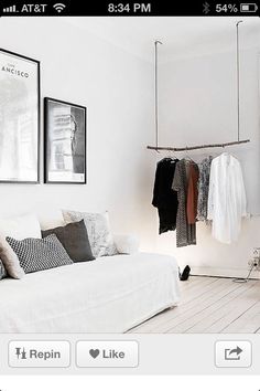 a living room with white furniture and clothes hanging on the rack in front of it