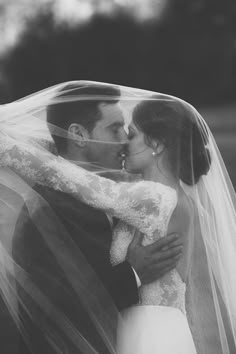 a bride and groom kissing under the veil of their wedding dress in black and white