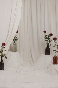 three vases with roses in them are sitting on a white sheeted table cloth