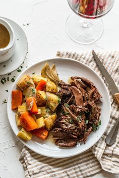 a white plate topped with roast, potatoes and carrots next to a glass of wine