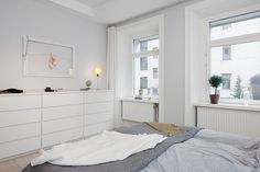 a bedroom with white walls and flooring has a large bed in front of two windows