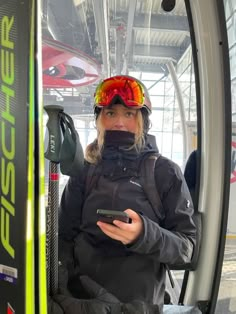 a woman sitting in a bus holding a cell phone and looking at the camera with goggles on