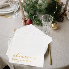 a table with place settings and napkins on it, along with pine branches in the background