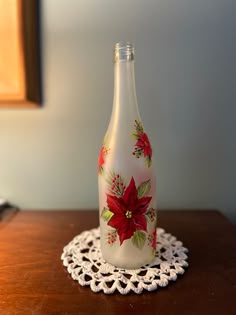 a glass bottle sitting on top of a table next to a doily with a poinsettia painted on it