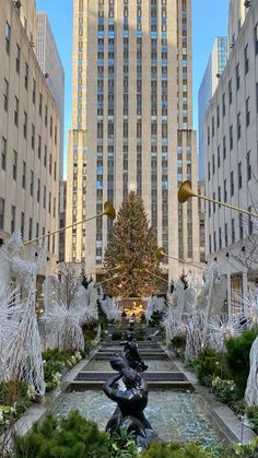 a christmas tree is in the middle of a garden with statues and trees around it