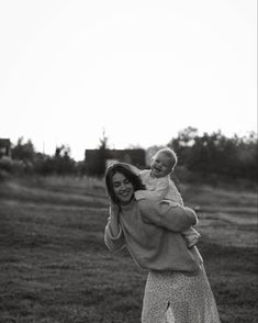 a woman holding a baby in her arms while standing on top of a grass covered field