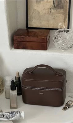 a brown purse sitting on top of a counter next to bottles and other items in front of a painting