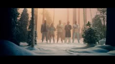 four people standing in the middle of a snowy forest