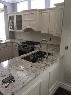 a kitchen with white cabinets and marble counter tops, an island sink and a phone on the counter